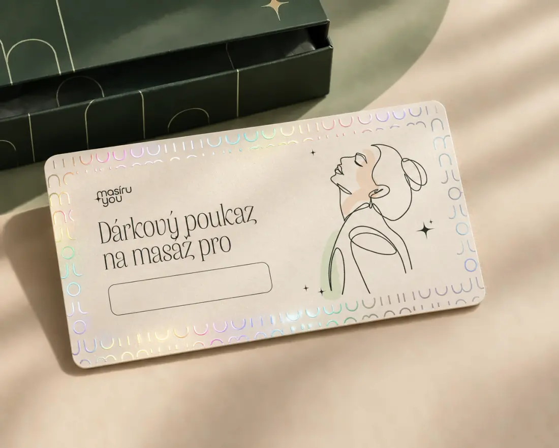 Tištěný dárkový poukaz Masíruyou s holografickým lemem leží před pootevřenou zelenou dárkovou krabičkou